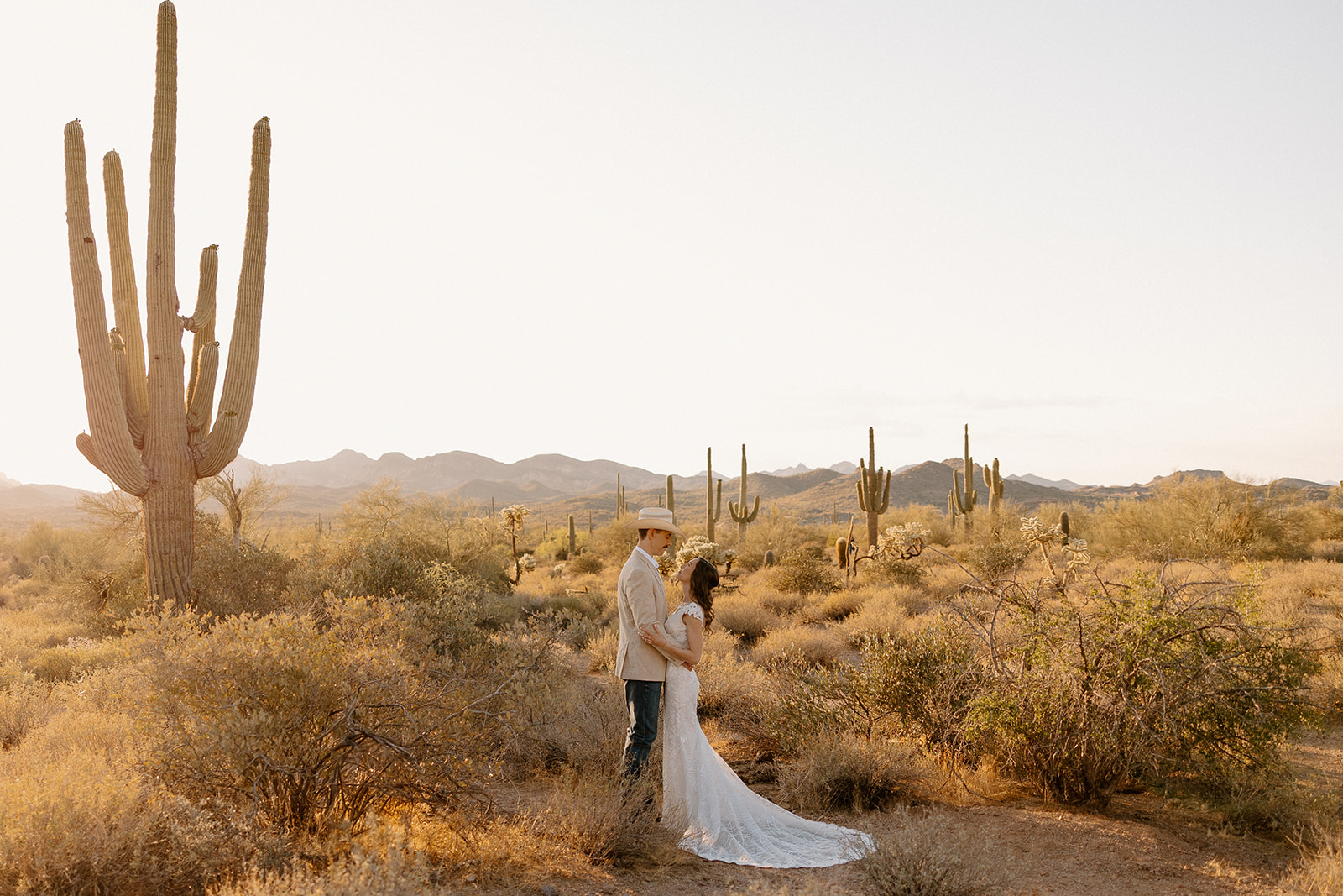 Bride and groom standing among saguaro cacti as they elope in Arizona at sunset.
