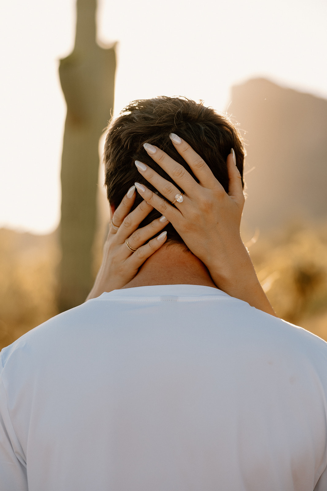 Close-up of bride’s hands resting on groom’s neck in warm desert light.