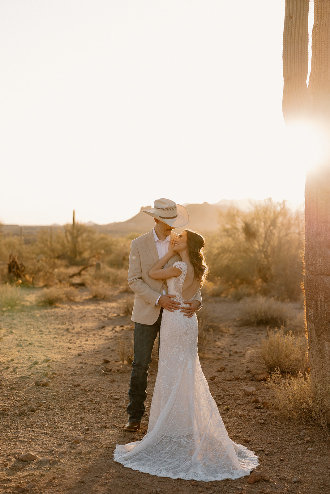 Couple standing in warm sunset light beside tall desert cacti during their Arizona elopement.