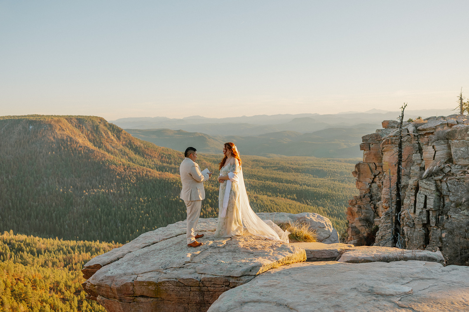 Couple exchanging vows on a cliff at sunset overlooking endless mountain ridges.