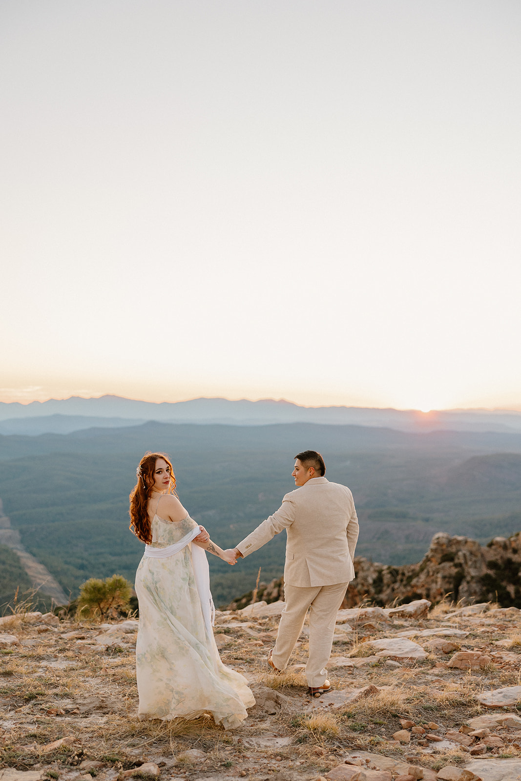Couple walking hand in hand across a mountain overlook at sunrise after they elope in Arizona.