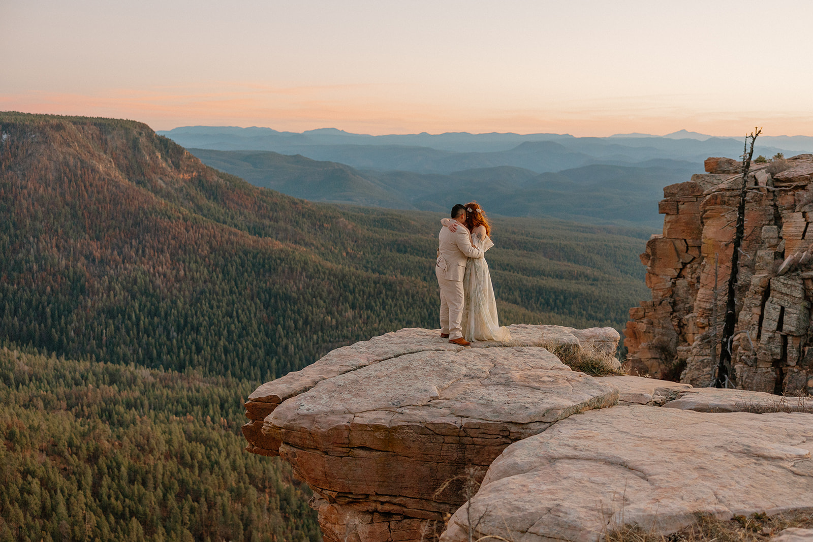 Couple standing on a cliff overlook at sunset as they elope in Arizona with sweeping mountain views.