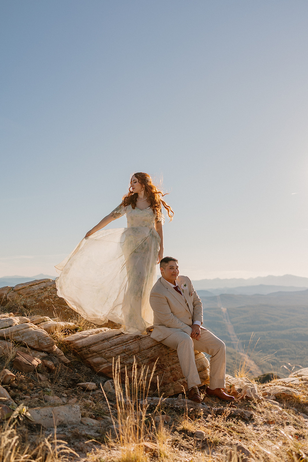 Bride lifting her dress in the wind beside groom on a mountain overlook as they elope in Arizona.