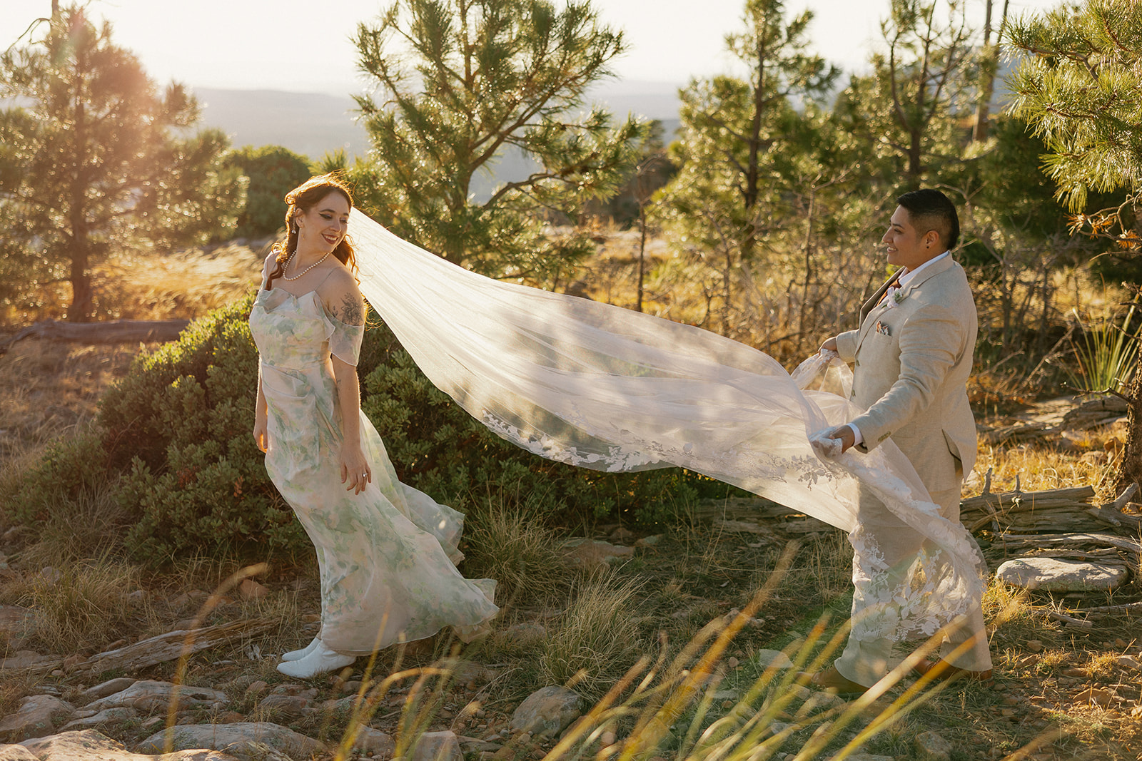 Bride's veil blows in the wind as her partner helps lift it. 