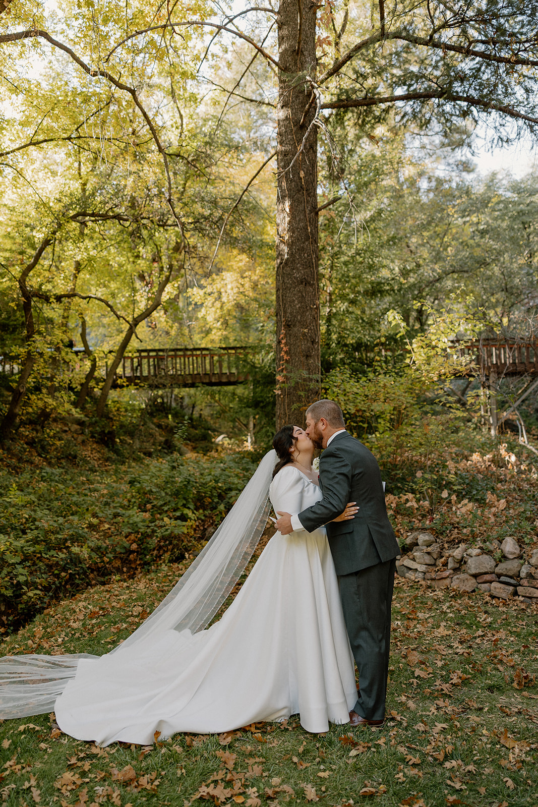 Bride and groom kissing beneath tall trees during a romantic forest elopement.