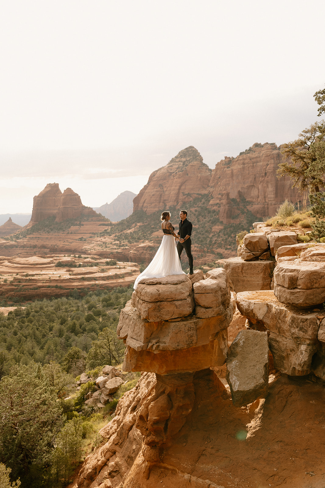 Bride and groom standing on a dramatic cliff edge at sunset after choosing to elope in Arizona.