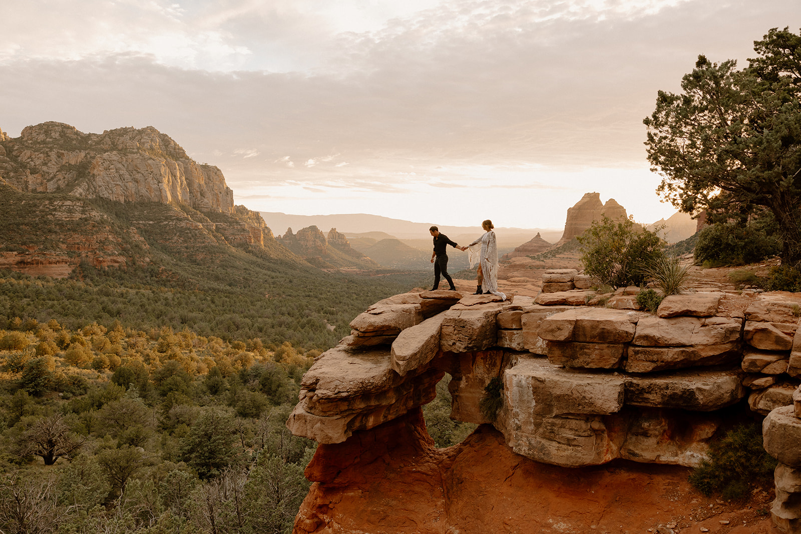 Couple holding hands on a red rock overlook while they elope in Arizona at sunset.