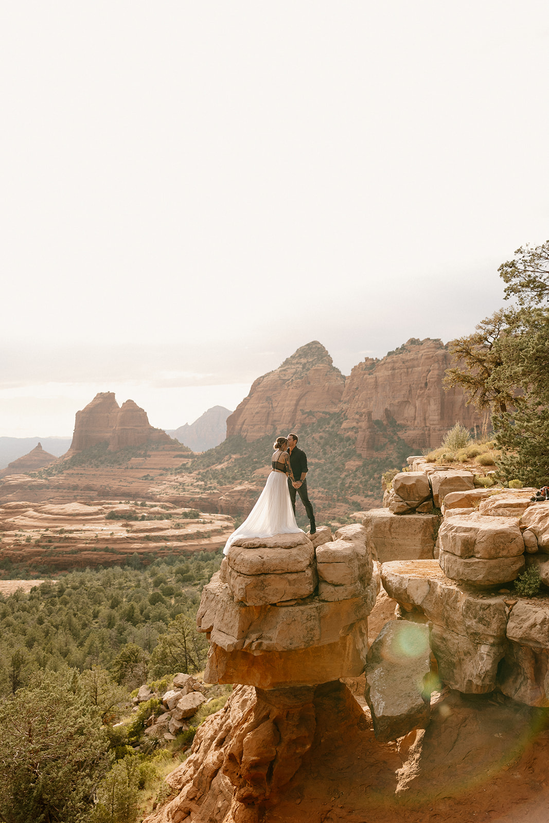Couple standing on a dramatic red rock cliff at sunset as they elope in Arizona.
