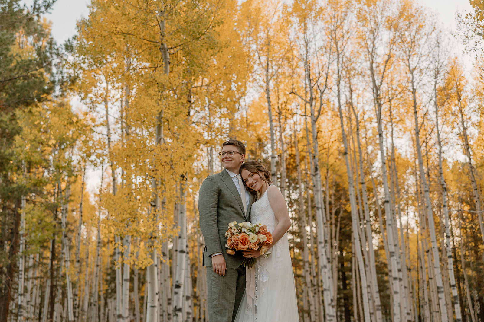 Newly married couple embracing in golden aspens during golden hour smiling with joy. 