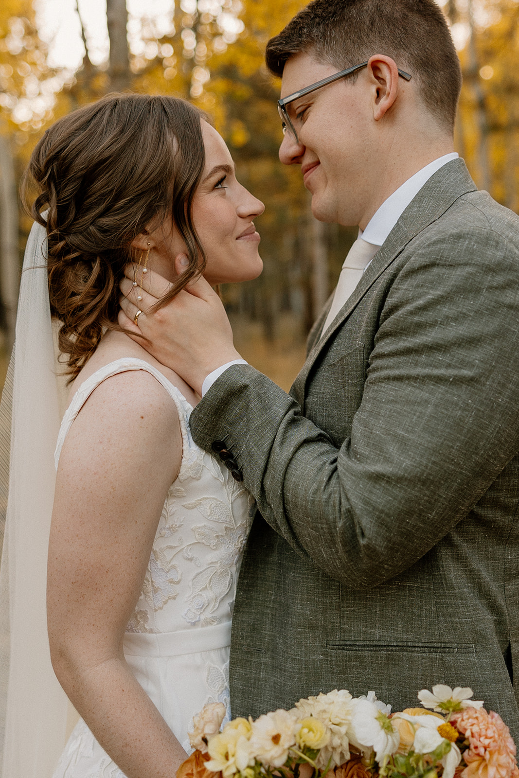 Couple in formal black wedding attire embracing in a quiet pine forest clearing.