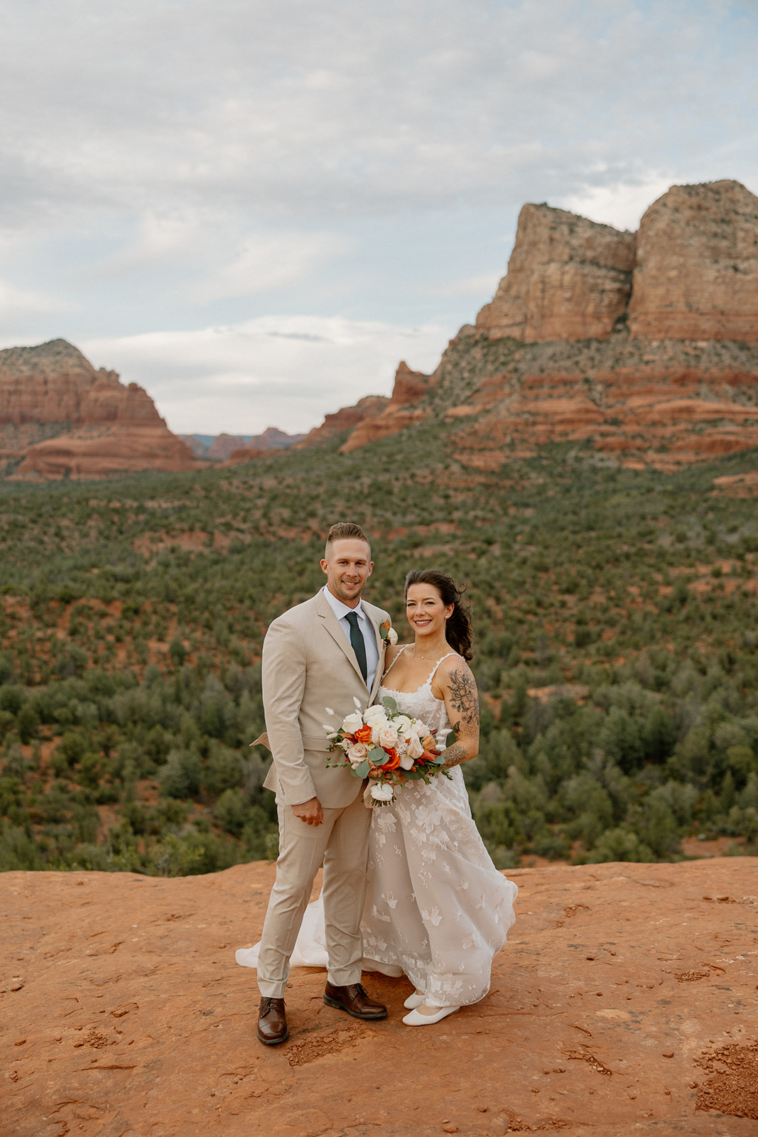 Newly married couple smiling together on red rock overlooking beauitful Arizona elopement locations. 