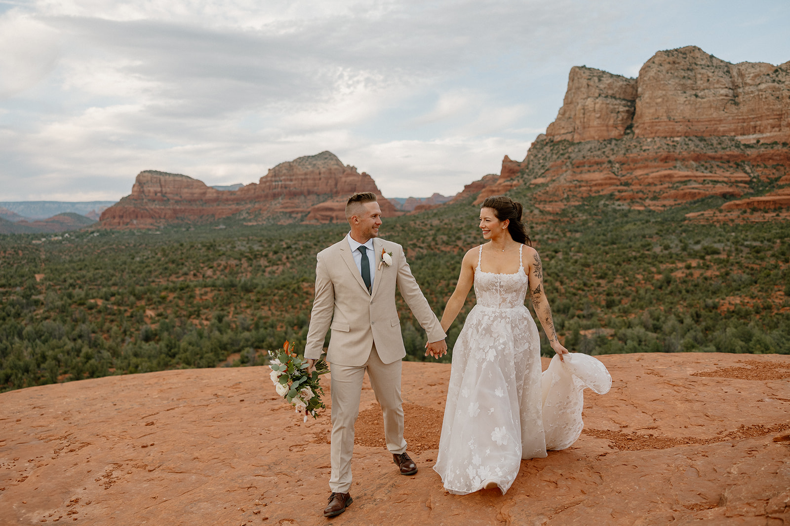 Bride and groom holding hands on a red rock cliff as they elope in Arizona.