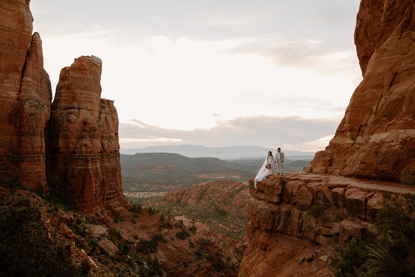 Couple standing on a cliff between towering canyon walls while they elope in Arizona.