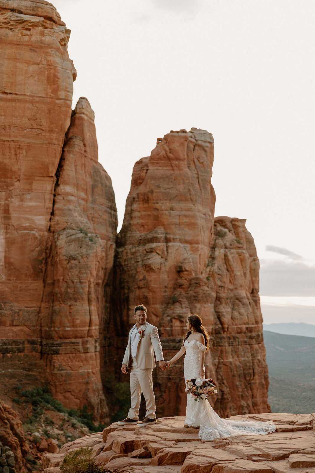 Bride and groom holding hands beneath towering sandstone formations as they elope in Arizona.
