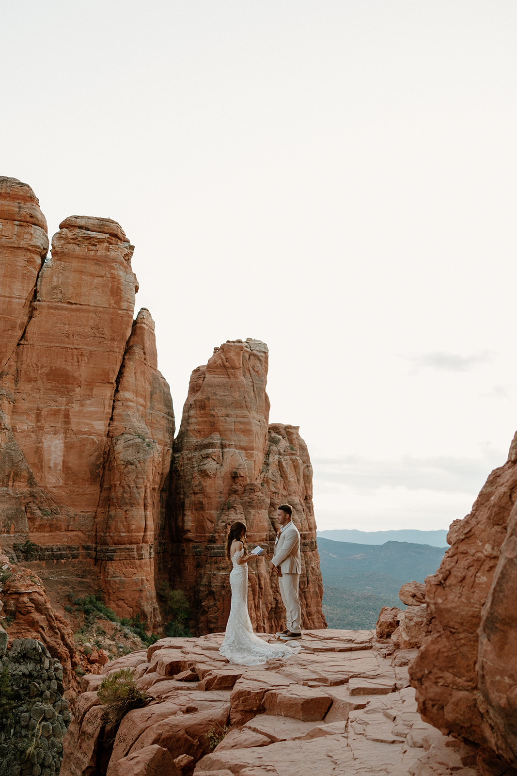 Bride and groom standing between towering red rock formations as they elope in Arizona.