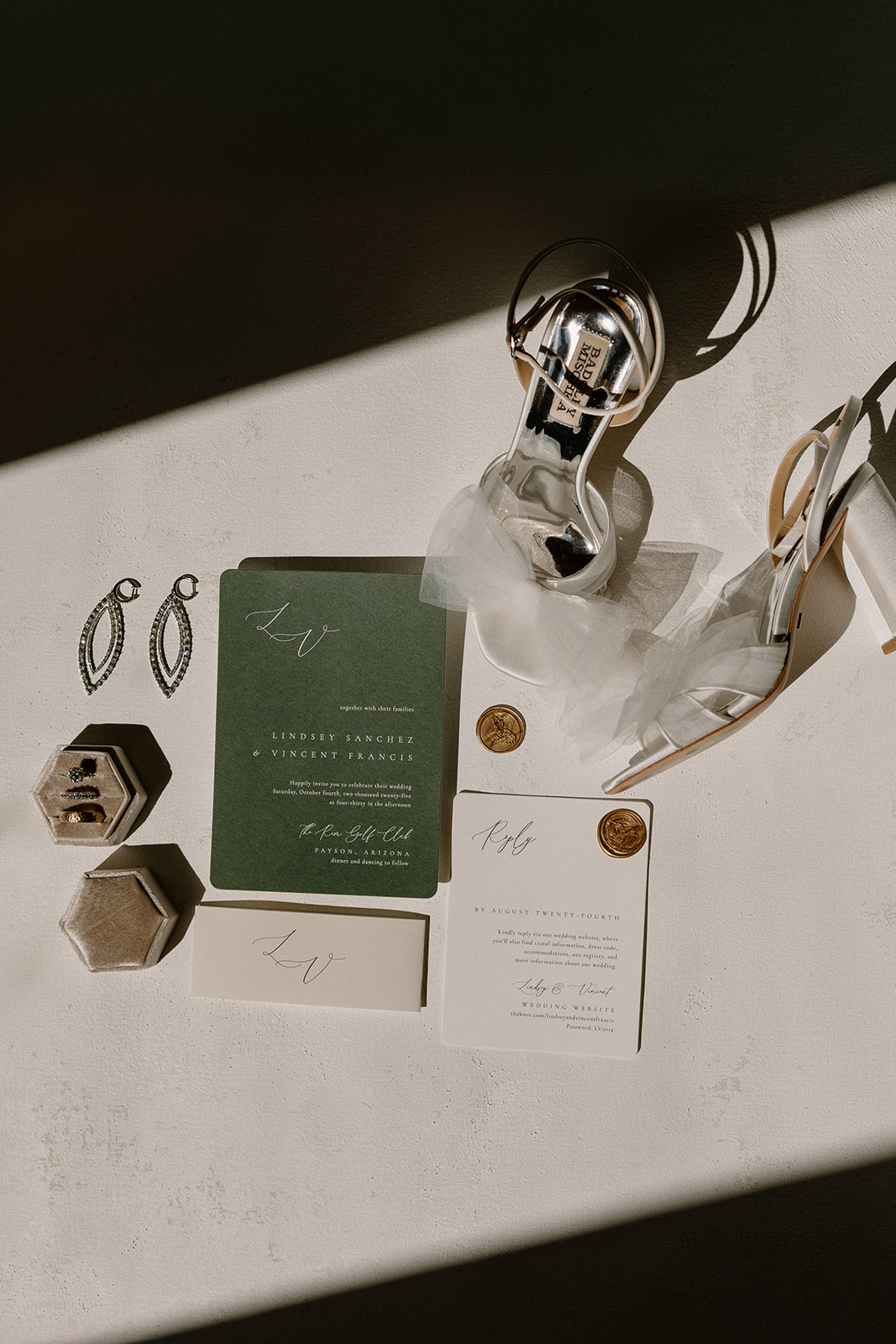 Wedding flat lay featuring invitation suite, rings, earrings, and bridal heels styled in natural light.