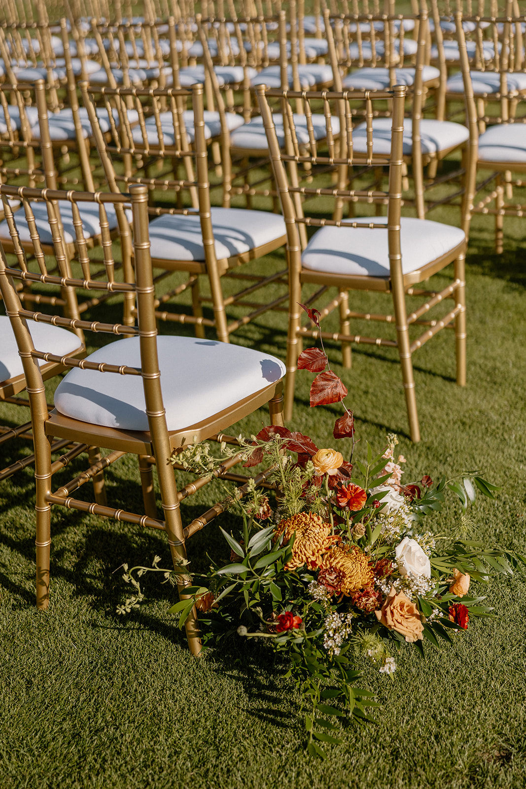 Rows of gold ceremony chairs with fall floral arrangements placed along the aisle at a Payson wedding venue.