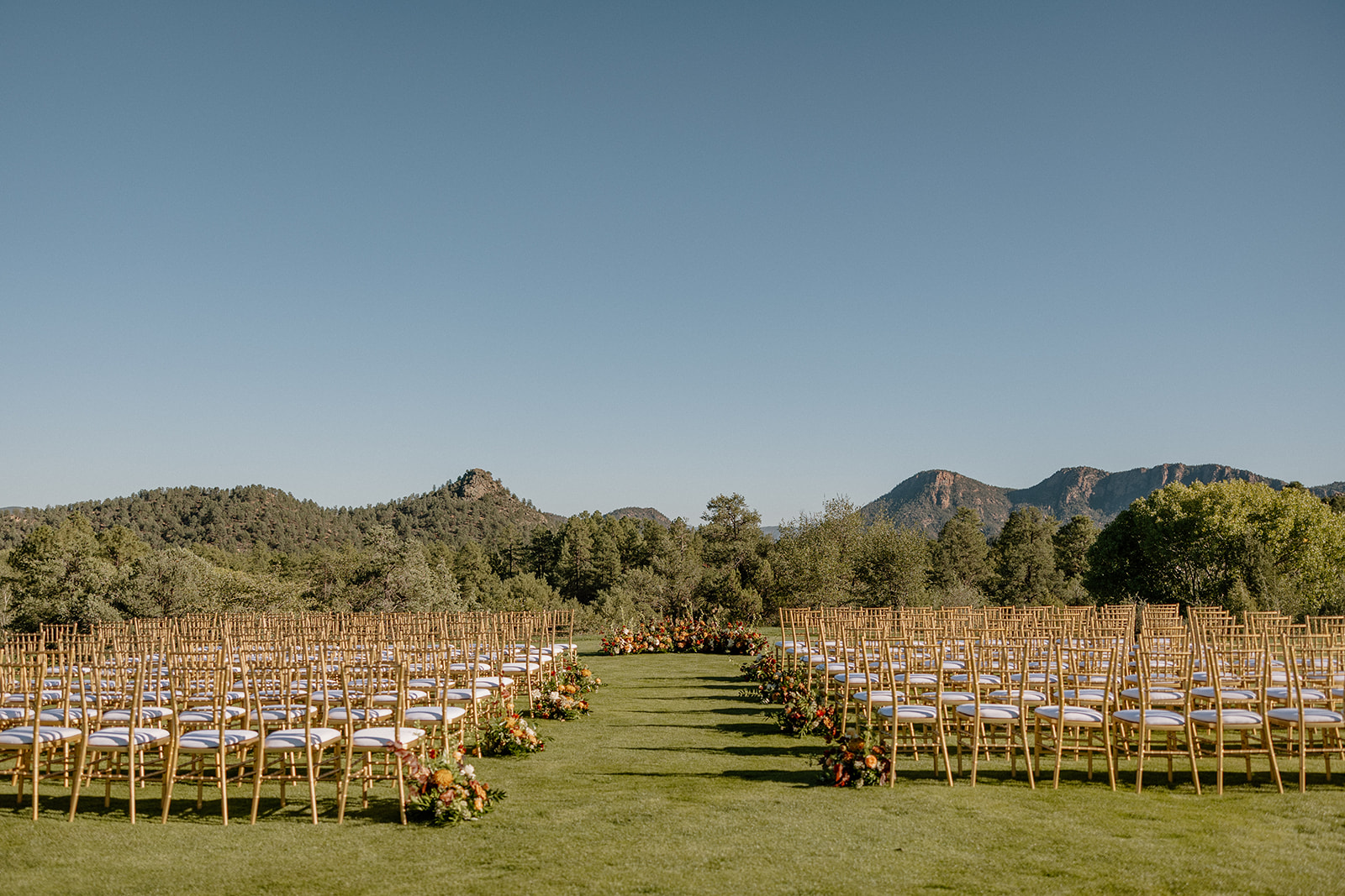 Wide view of an outdoor ceremony setup with gold chairs and mountain views at a Payson wedding venue.