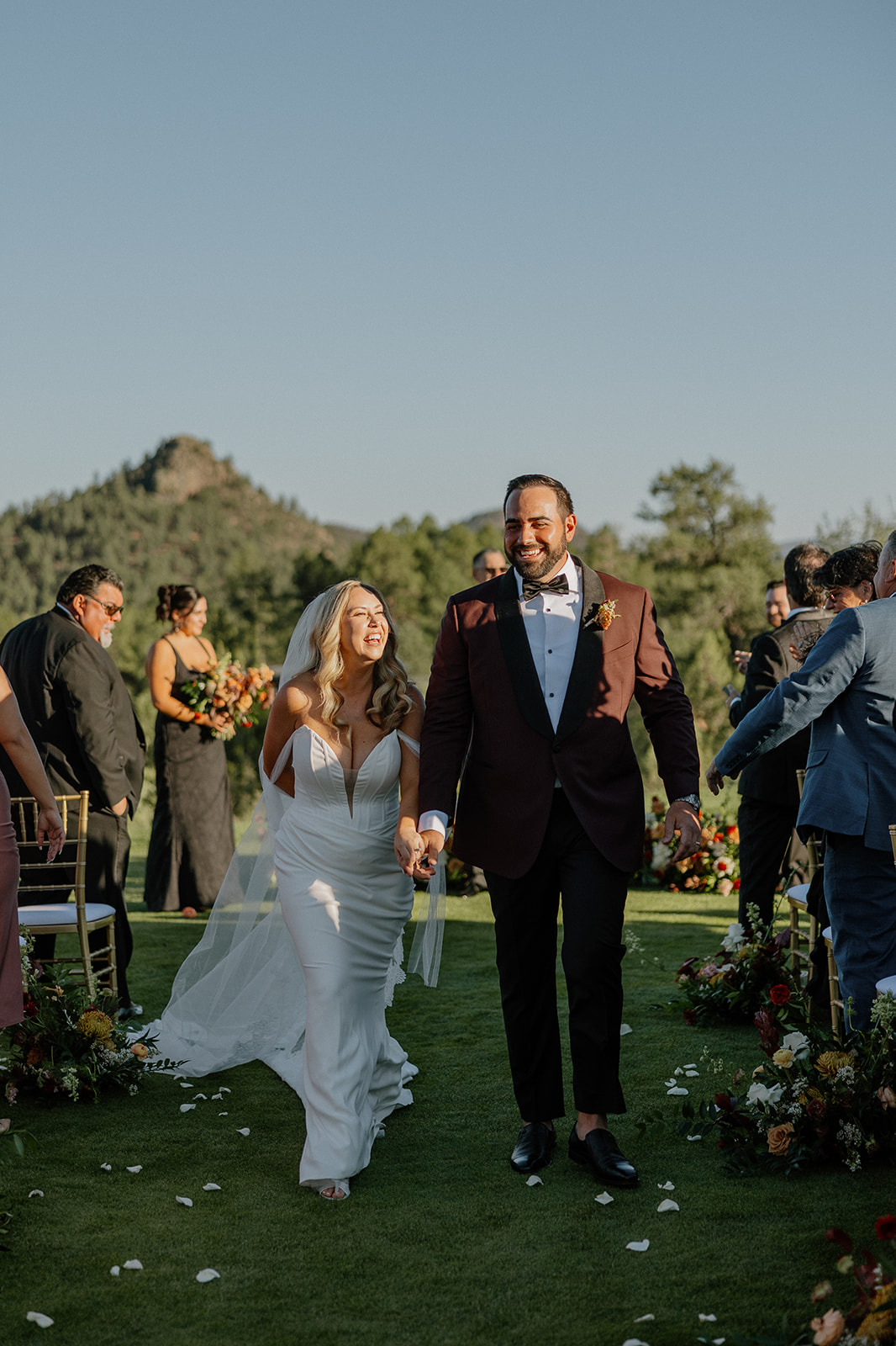Newlyweds walk back down the ceremony aisle smiling as guests cheer during an outdoor wedding celebration.
