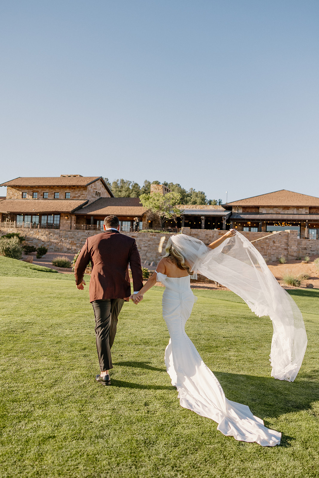 Bride and groom run hand in hand across the lawn, the bride’s veil flowing behind them at a Payson wedding venue.