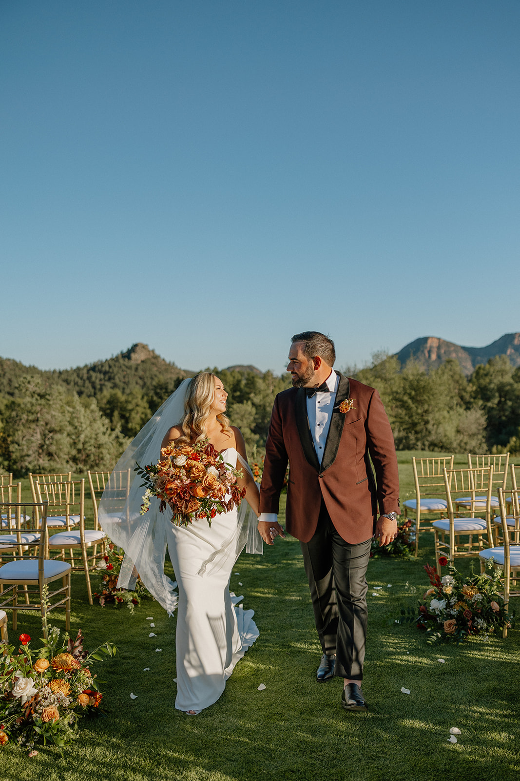 Newlyweds walk hand in hand down the ceremony aisle surrounded by florals at a Payson wedding venue.