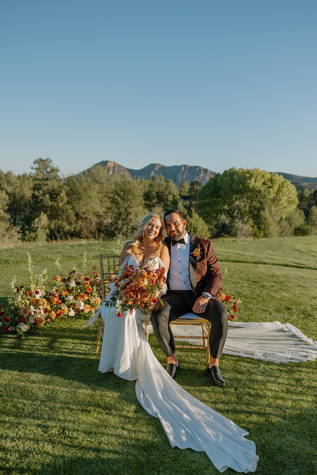 Bride and groom sit together on ceremony chairs surrounded by florals and mountain views at a Payson wedding venue.