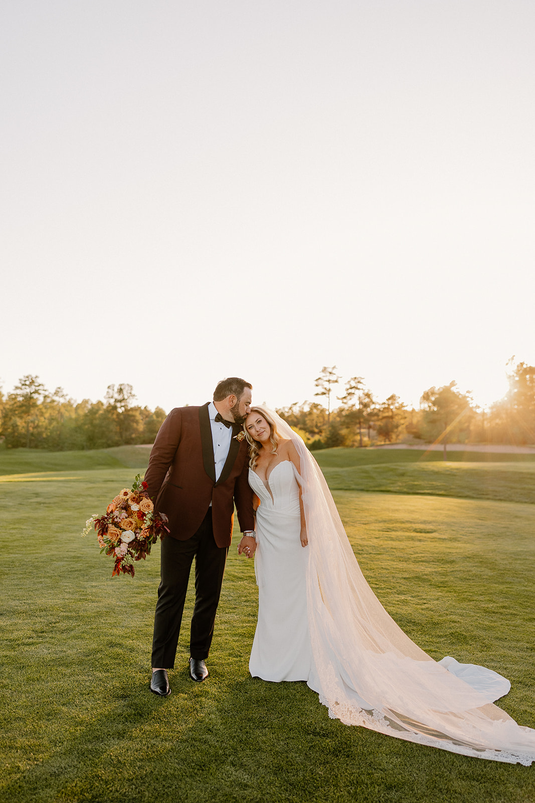 Couple shares a quiet golden hour moment on the lawn, the bride’s veil flowing behind them.