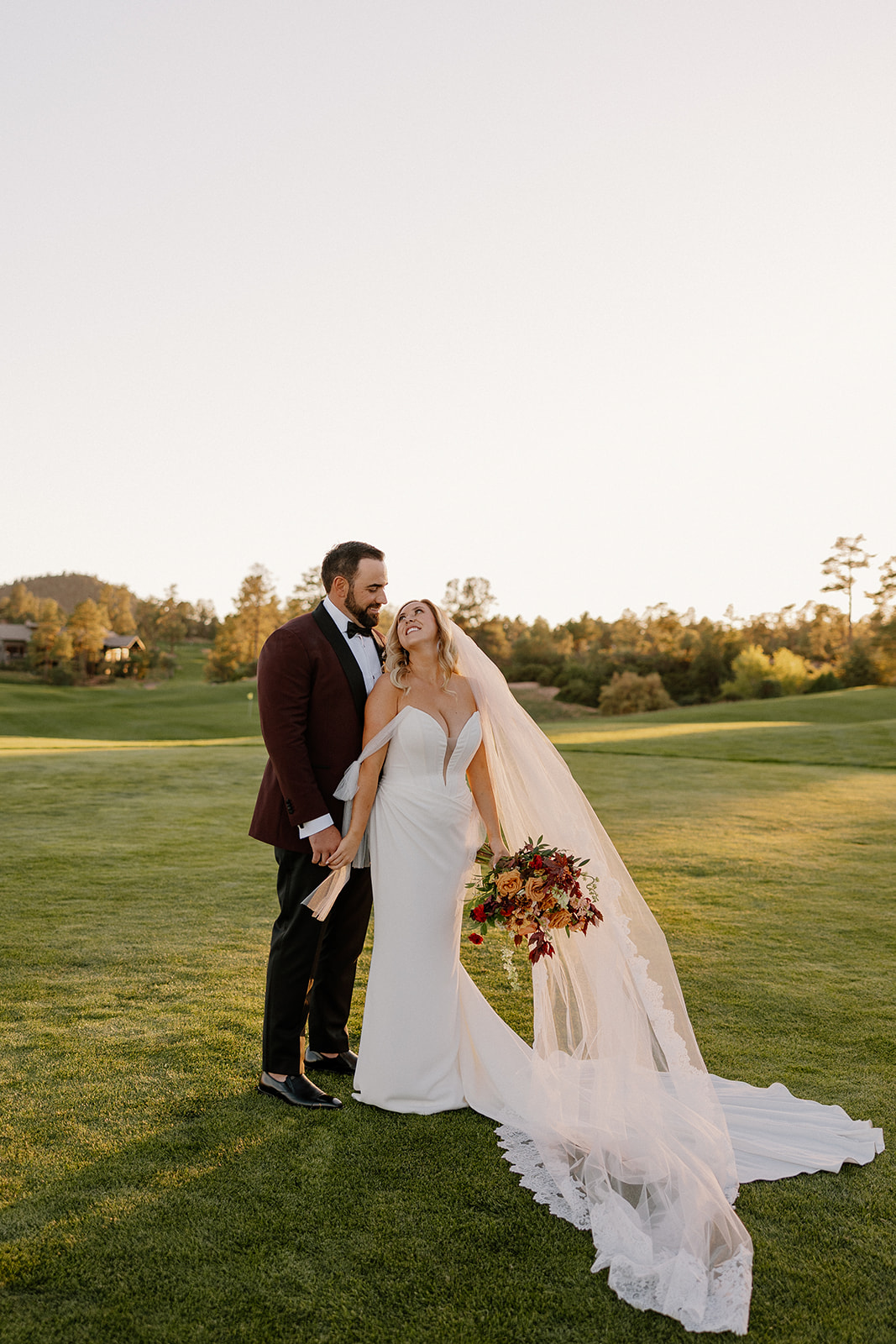 Bride and groom stand hand in hand on a lush green lawn during golden hour portraits at a Payson wedding venue.