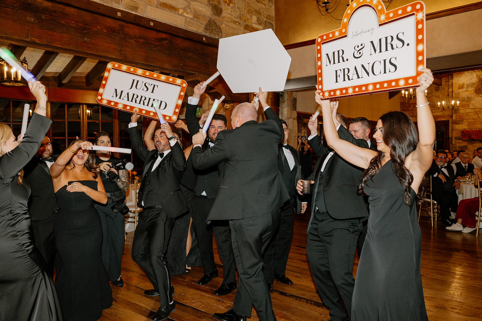 Wedding party celebrates on the dance floor holding “Just Married” signs during a lively reception moment.