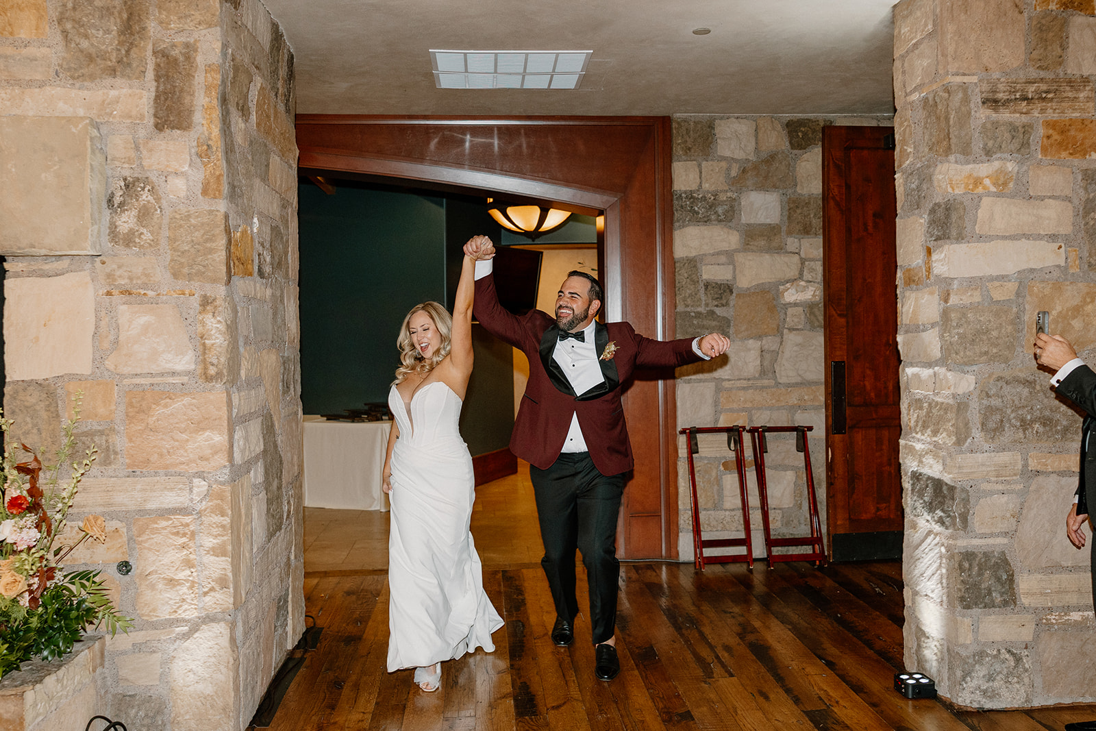 Newlyweds make a joyful grand entrance into their reception inside a Payson wedding venue with stone walls and wood floors.