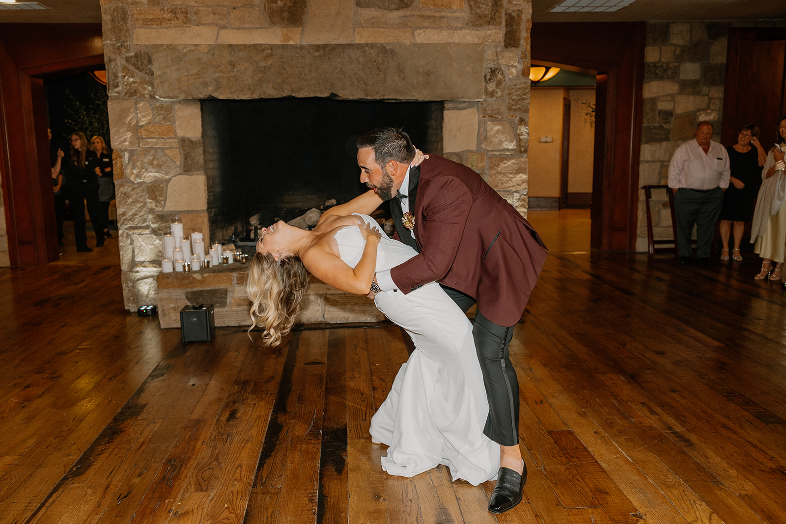 Groom dips the bride during their first dance in front of a stone fireplace at a Payson wedding venue.