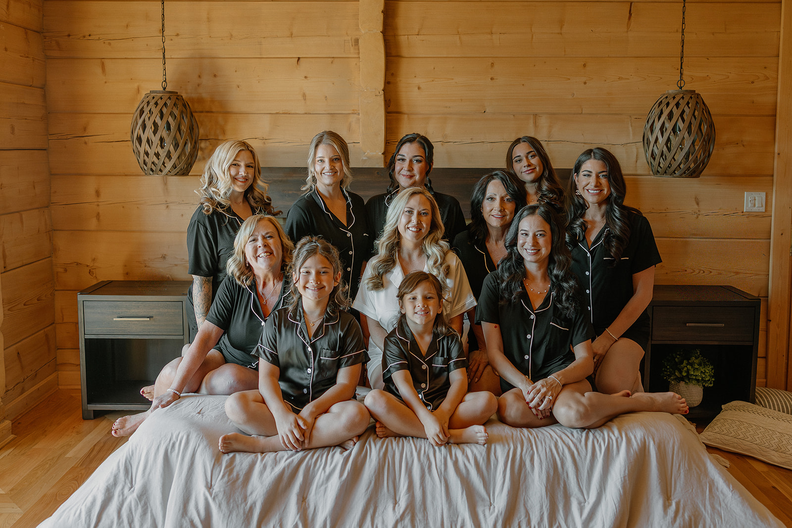 Bride sits on a bed surrounded by bridesmaids in matching pajamas during morning wedding preparations.