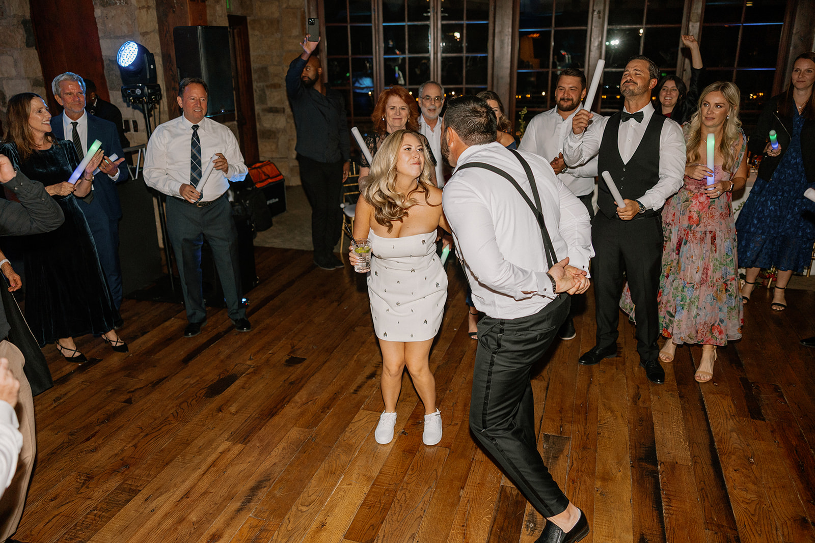 Bride and groom dance together on the wooden dance floor as guests cheer them on during an energetic reception.