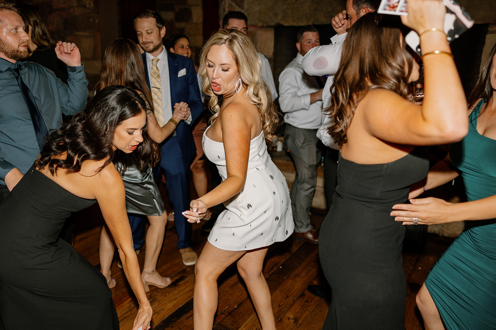 Wedding guests dance joyfully on the reception floor, celebrating late into the night with the bride at the center.