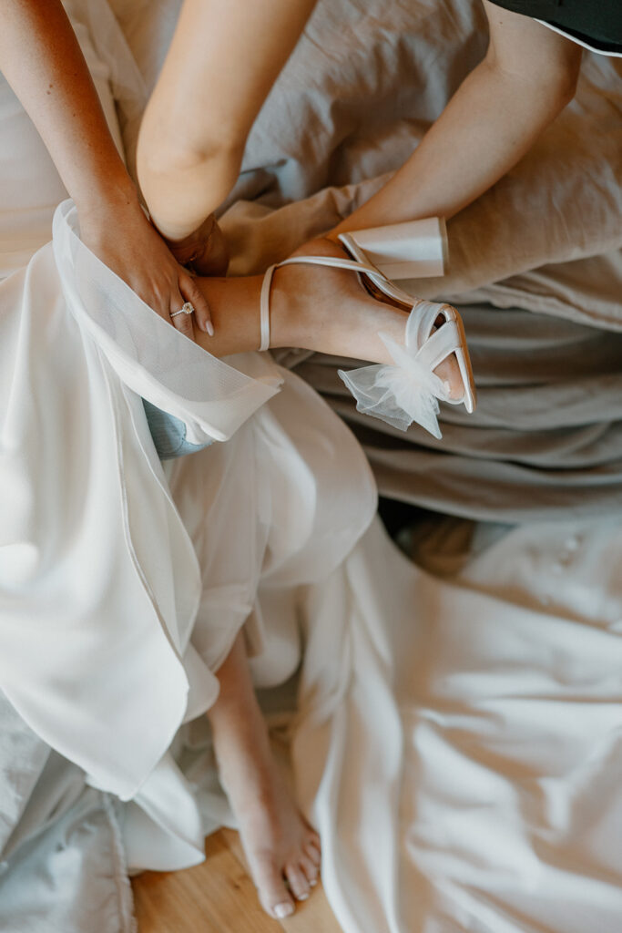 Close-up of the bride’s shoes being put on beneath flowing fabric during wedding day preparations.