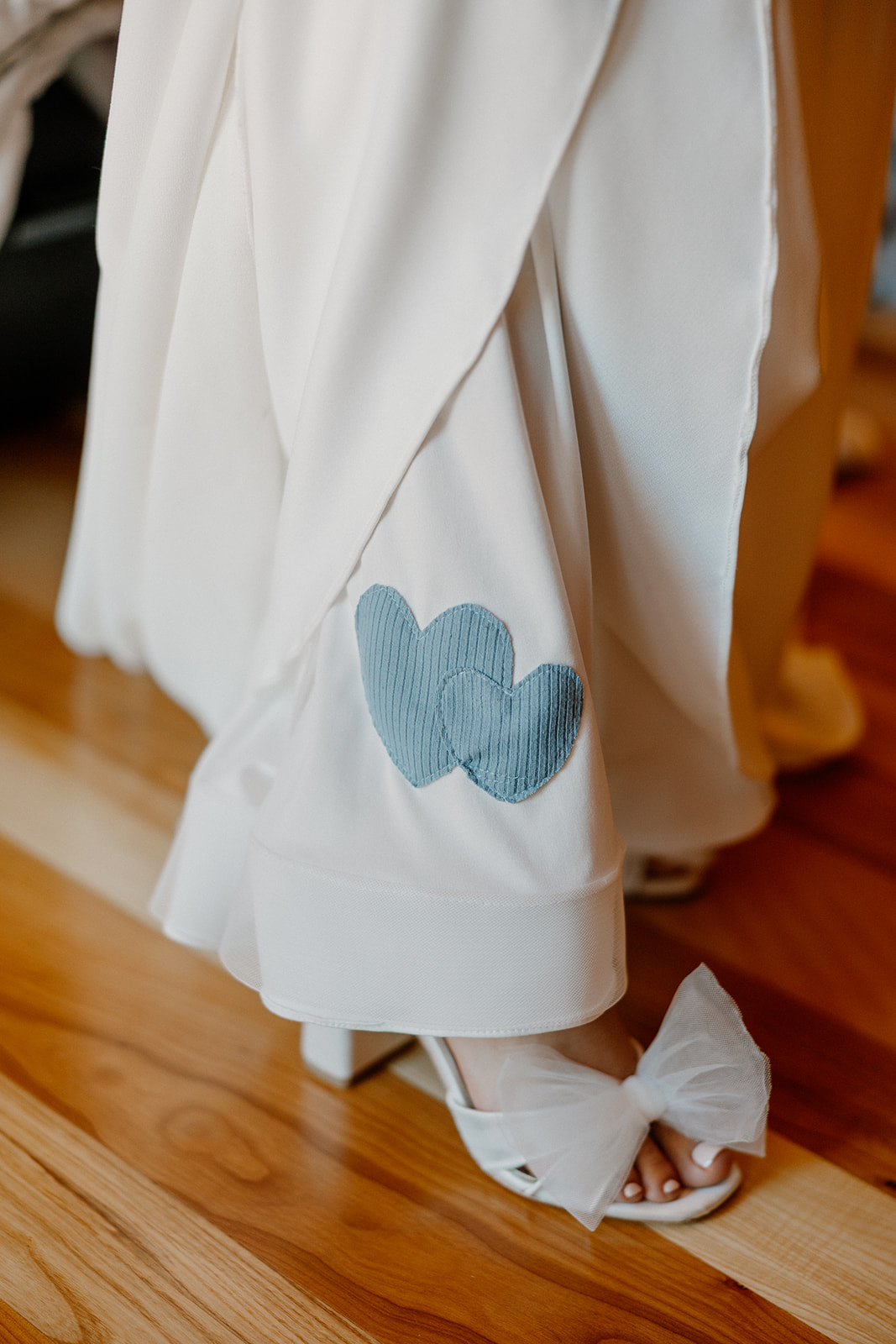 Close-up of embroidered hearts on the bride’s robe and white heels during getting-ready moments.