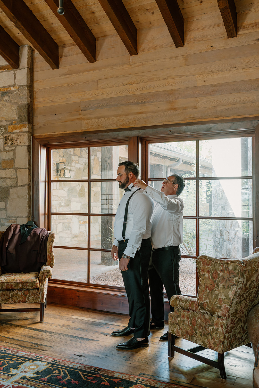 Father fastens the groom’s suspenders during a quiet getting-ready moment inside a Payson wedding venue.