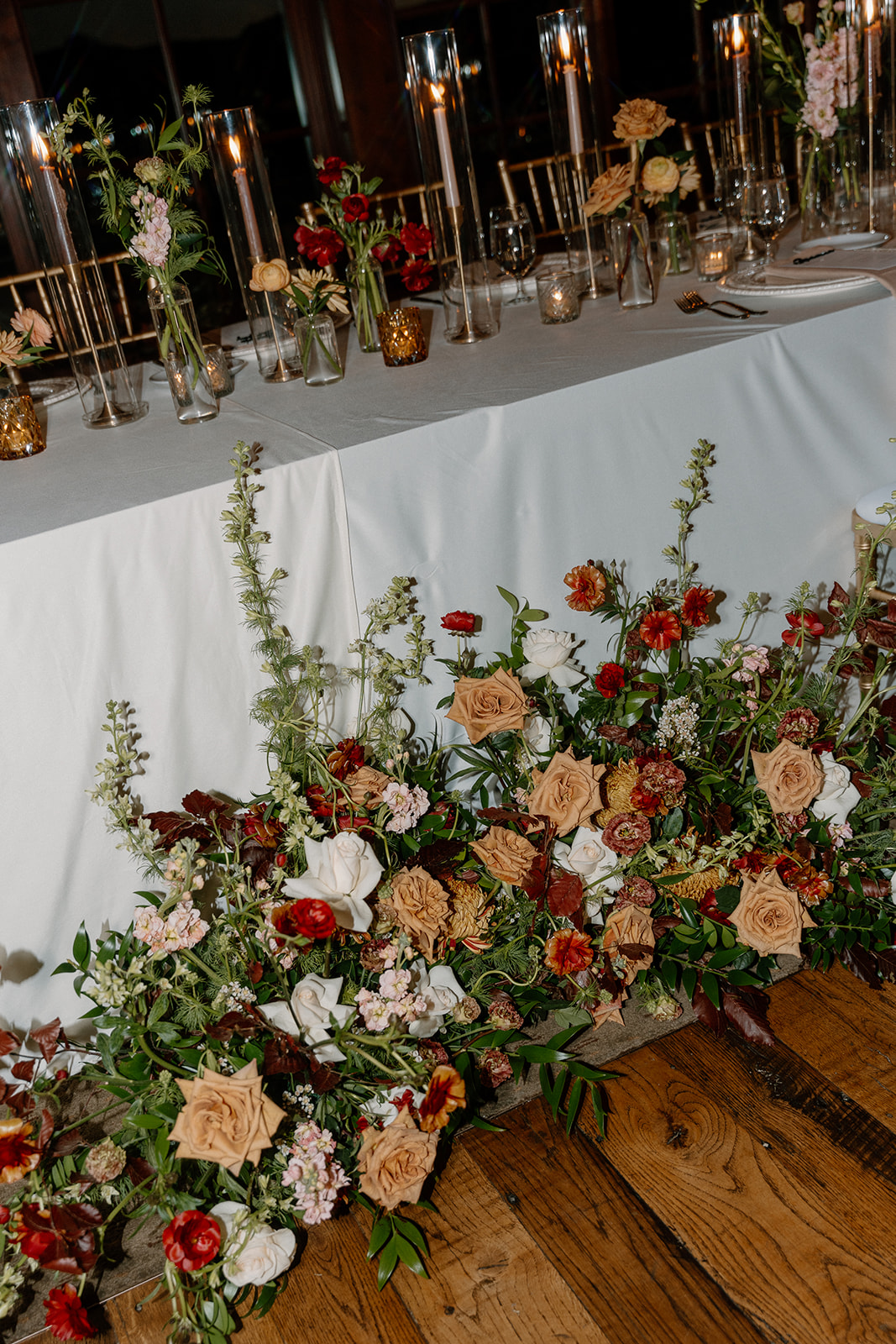 Floral head table arrangement with fall-toned flowers and candles styled inside a Payson wedding venue reception space.