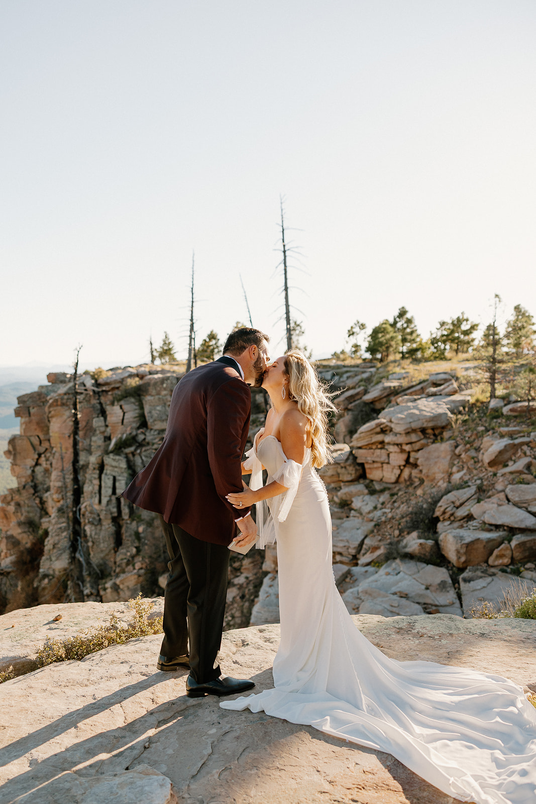 Bride and groom share a kiss on a rocky cliff overlook during sunset portraits in the Arizona mountains.