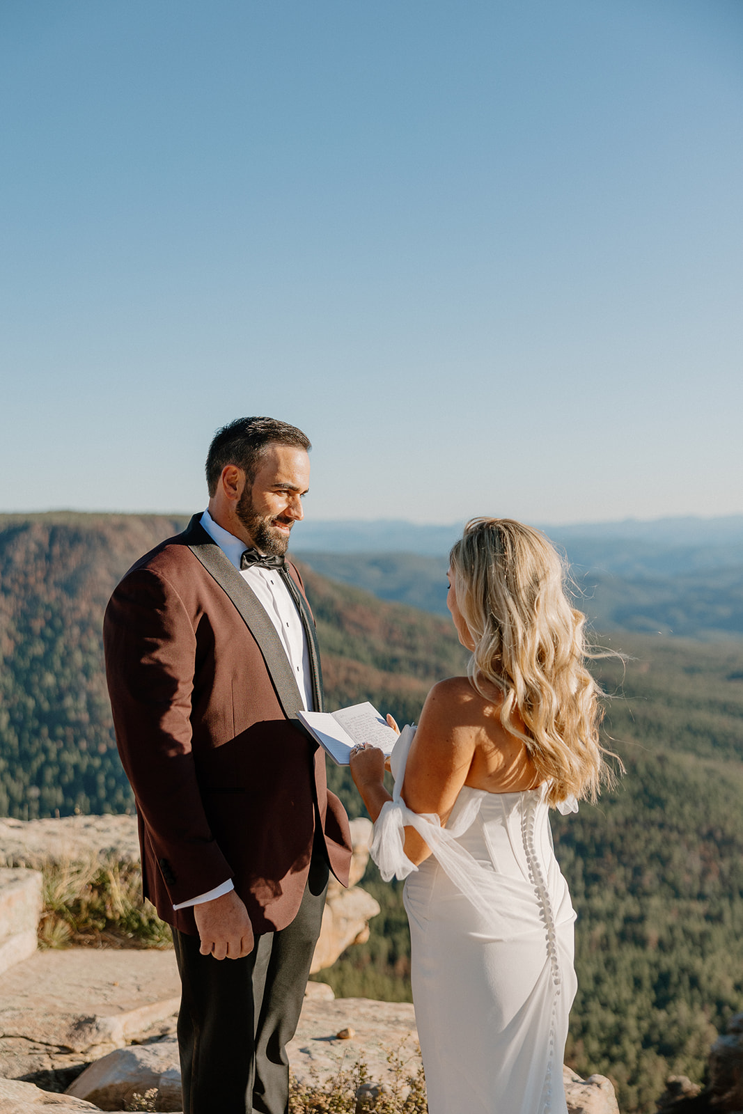 Bride reads her vows to the groom on a cliffside with sweeping forest views at a Payson wedding venue.
