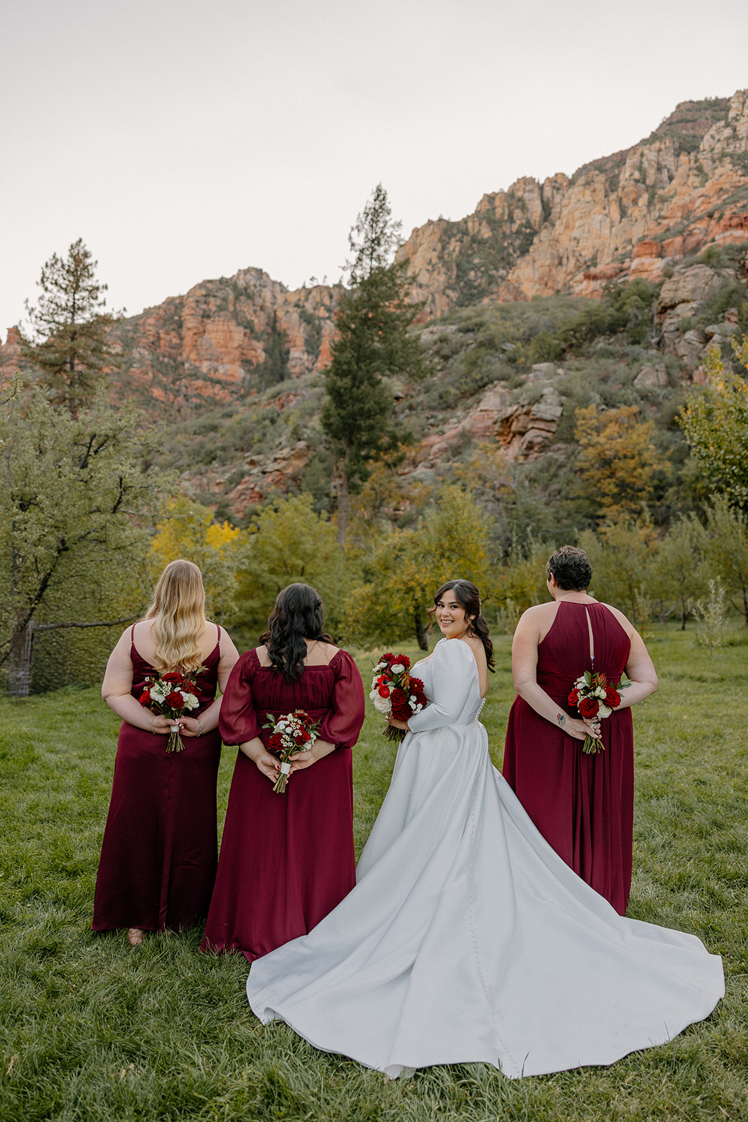 Bride posing with bridesmaids in burgundy dresses at a Sedona wedding venue with red rock backdrop