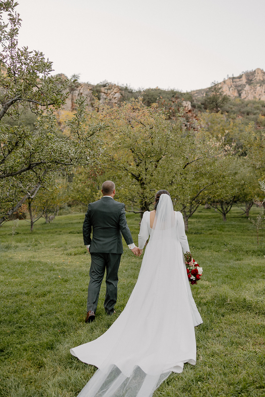Bride and groom walking away together through an orchard at a Sedona wedding venue