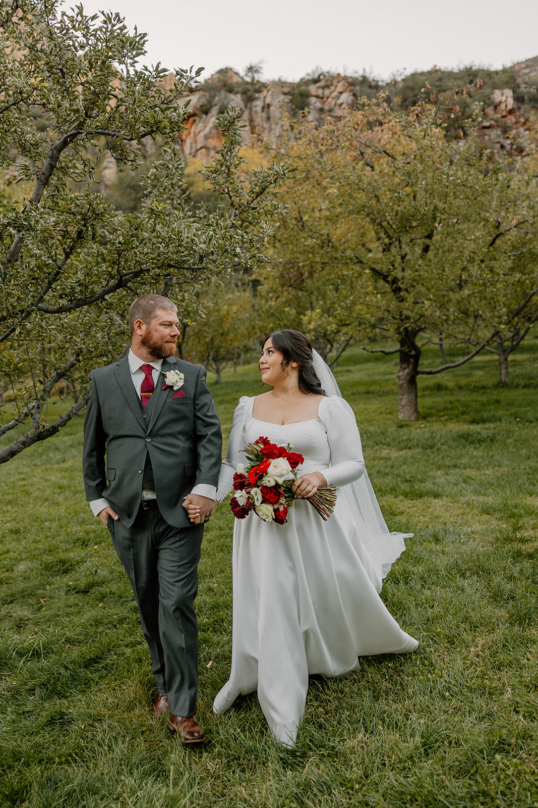Bride and groom walking hand in hand through an orchard at Orchard Canyon on Oak Creek