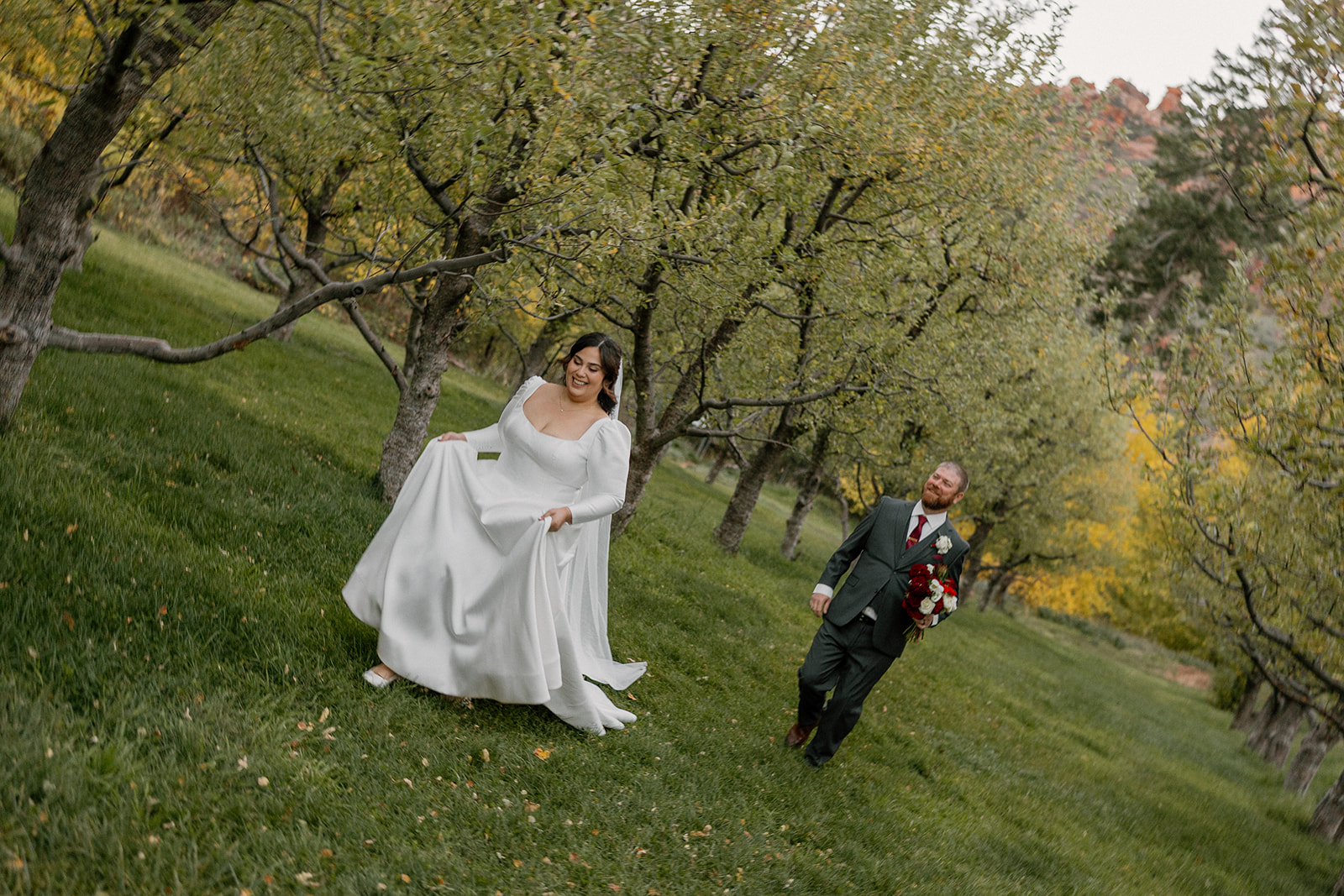 Bride and groom walking through an orchard together at a Sedona wedding venue during golden hour