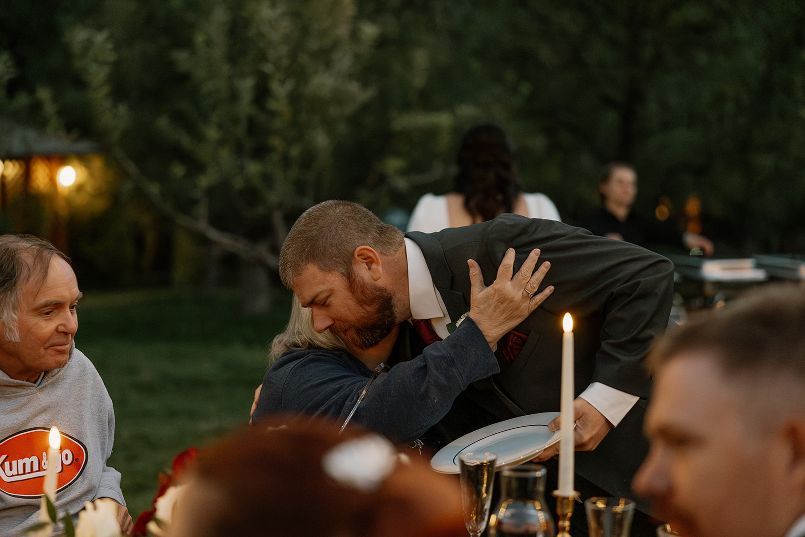 Groom hugging a guest during dinner at a Sedona wedding venue, surrounded by candlelight and long tables outdoors