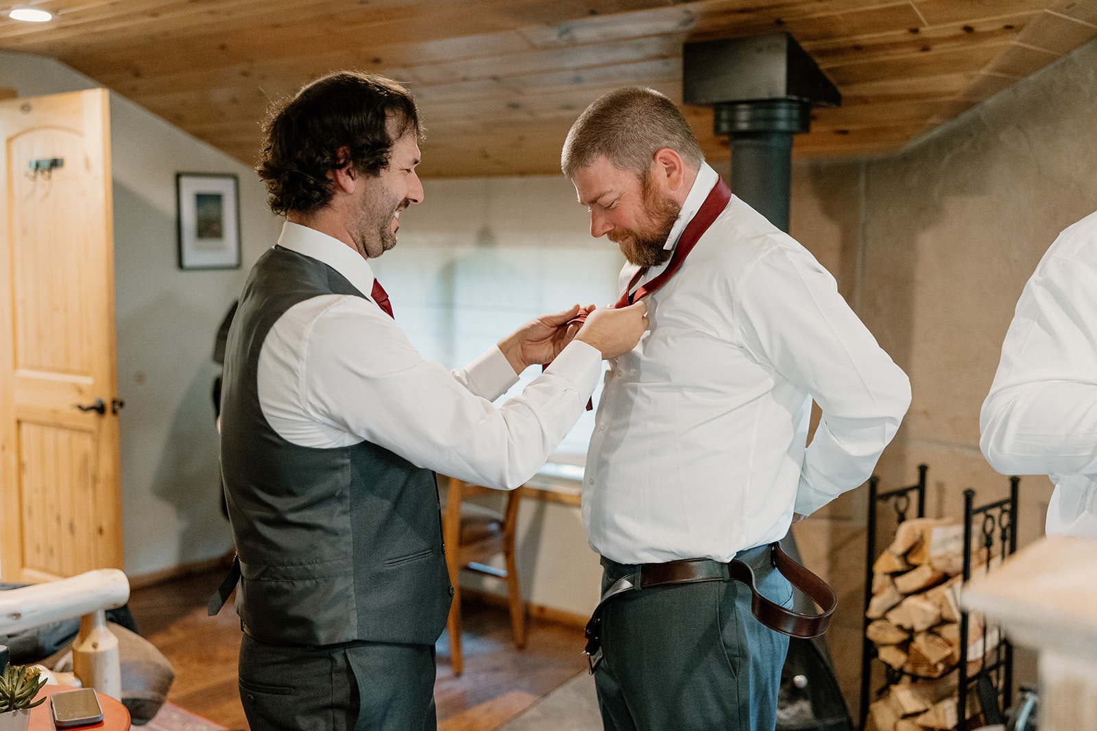 Groom laughing with groomsmen while getting ready inside a rustic cabin
