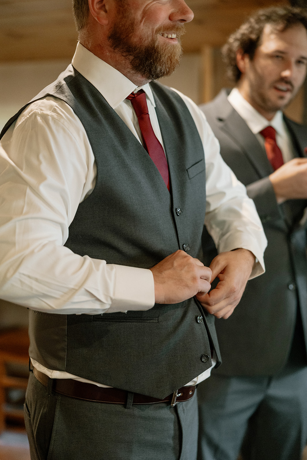 Groom buttoning his vest while getting ready indoors with groomsmen