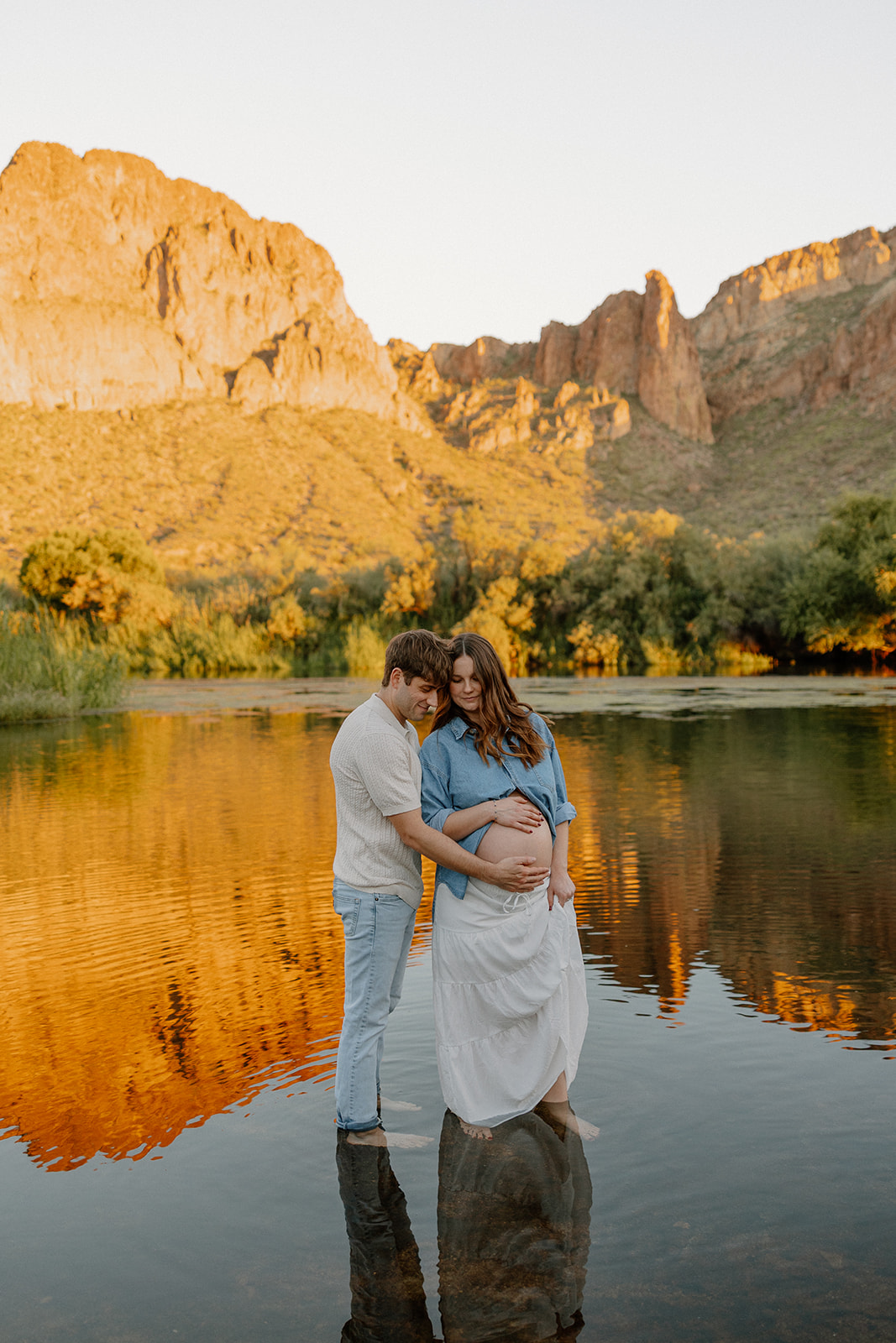 Couple holding hands in the water at sunset with mountains glowing in the background
