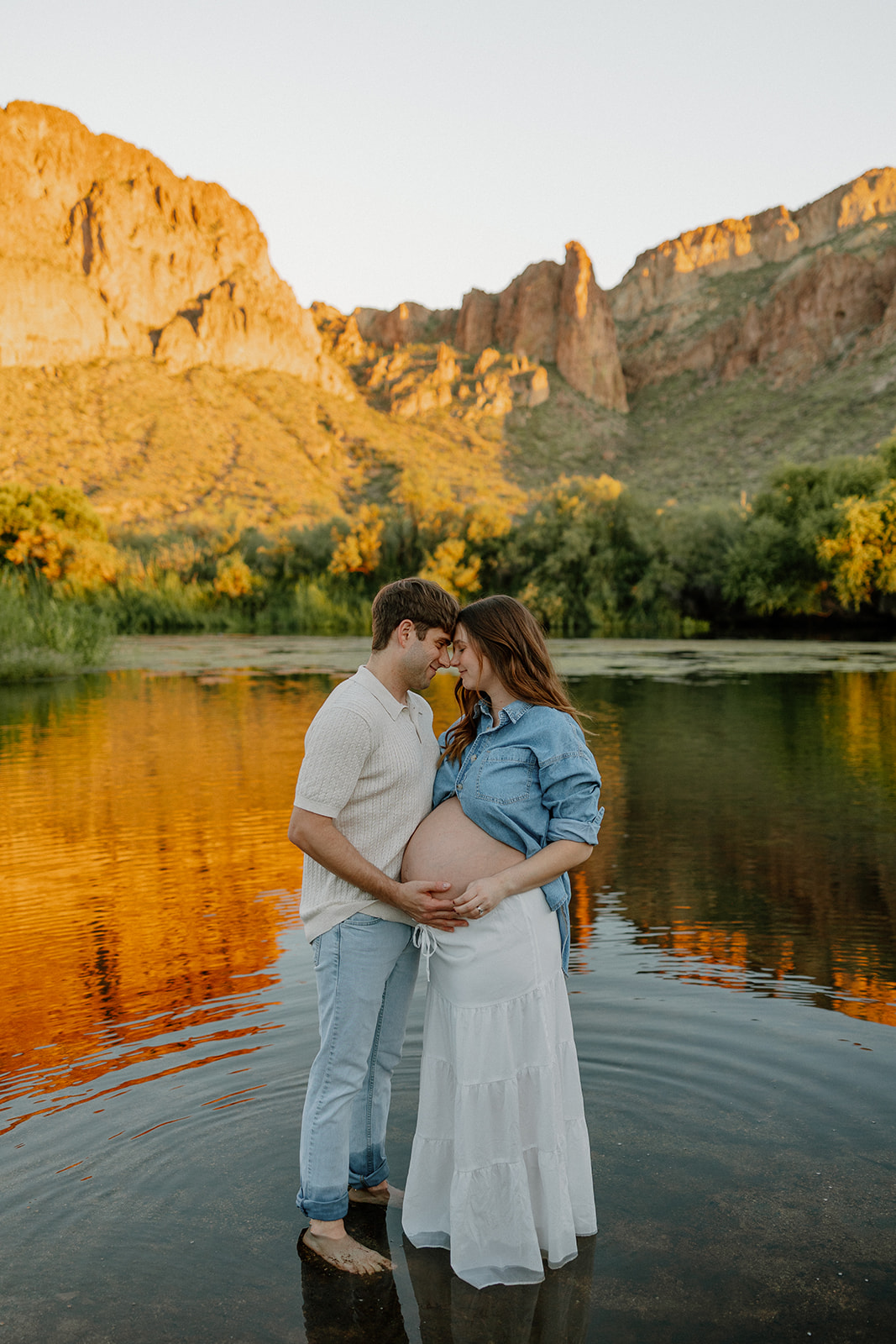 Couple standing together in the Salt River at sunset with warm mountain reflections, Arizona maternity photographer
