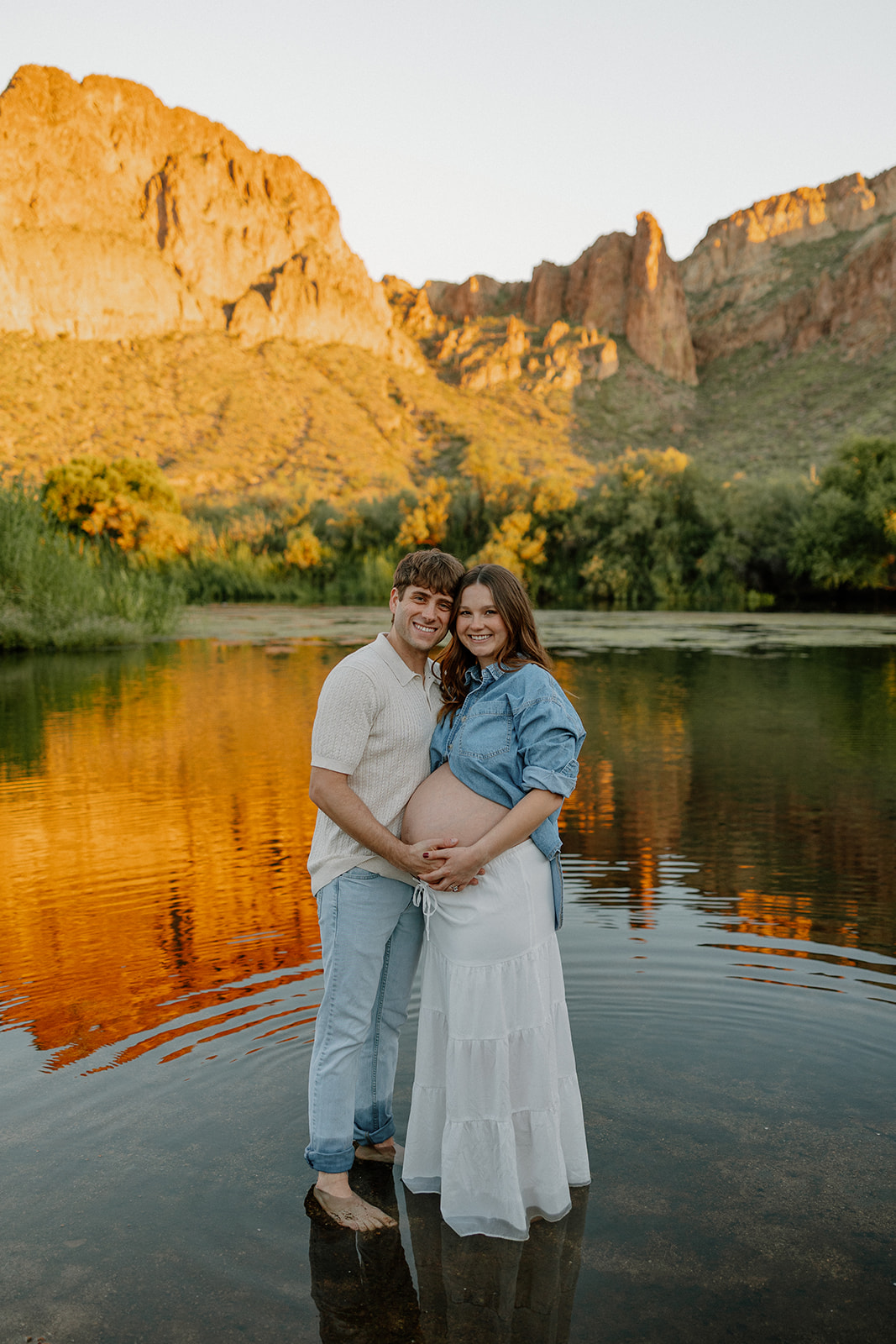 Couple standing together in the Salt River at sunset with glowing mountain reflections, Arizona maternity photographer
